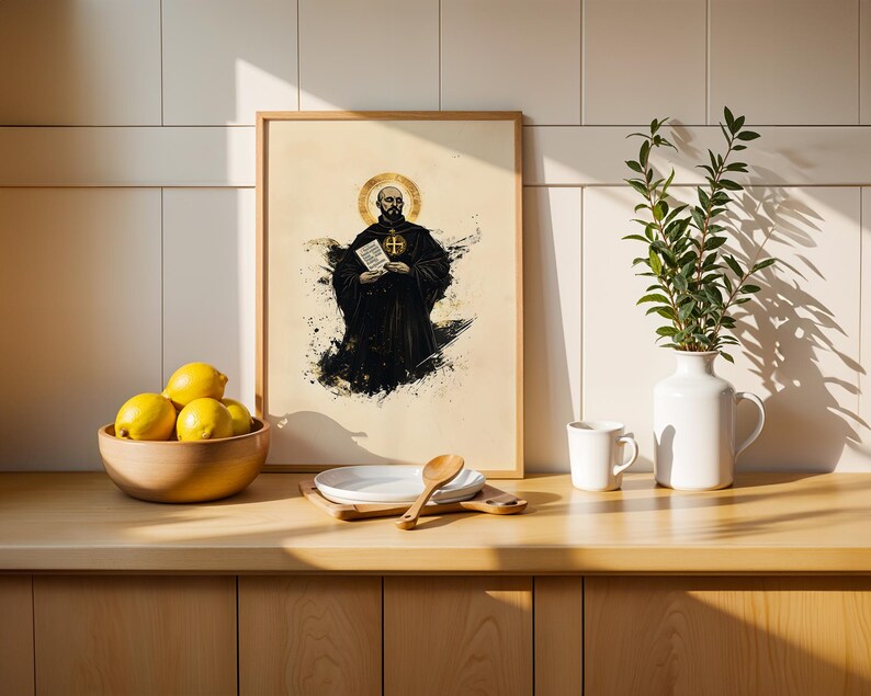 May include: A framed art print featuring a bearded figure in a black robe with a gold halo, holding a document with text. The illustration uses black ink splatters on a cream background. The frame is light wood, displayed on a kitchen counter.