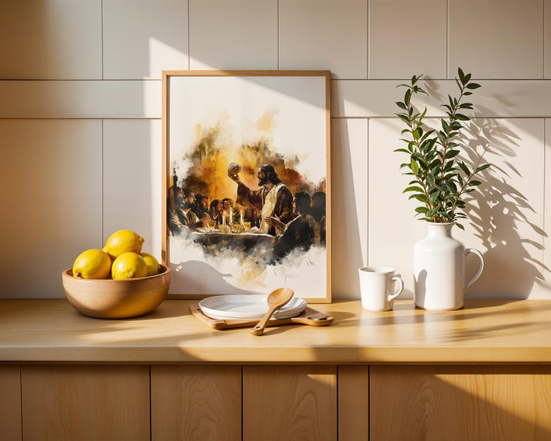 May include: A framed watercolour-style print depicting a group of people at a table with a central figure holding a round object, positioned next to a wooden bowl of yellow lemons, a stack of white plates with a wooden spoon, and a white vase with greenery.