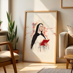 K&ouml;nnte beinhalten: Ein gerahmter Wandkunstdruck mit einer Aquarell-Illustration einer Nonne in schwarz-wei&szlig;em Habit. Die Figur h&auml;lt ein leuchtend rotes Buch, wobei ein rot-goldener Strahlenkranz hinter dem Kopf vor einem wei&szlig;en Hintergrund zu sehen ist.
