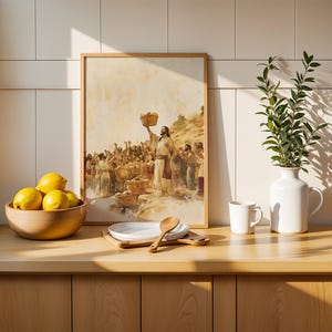 May include: A framed print depicting a biblical scene of a figure holding a basket above a crowd, placed next to a wooden bowl of yellow lemons, a stack of white plates with a wooden spoon, a white mug, and a white pitcher with green leaves.