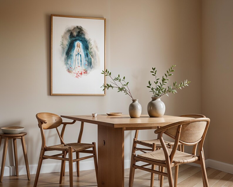Puede incluir: Una l&aacute;mina de acuarela enmarcada que representa una figura con t&uacute;nica blanca y azul con las manos juntas en oraci&oacute;n, rodeada por un aura azul oscuro y detalles florales rojos en la base, colgada sobre una mesa de comedor de madera.