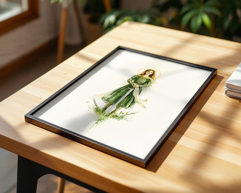 Op de afbeelding: Een ingelijste aquarelillustratie van een figuur in een groene jurk die een lang zwaard vasthoudt, met een gouden halo achter het hoofd en groene bladeren aan de basis, gepresenteerd in een dunne zwarte lijst op een licht houten oppervlak.