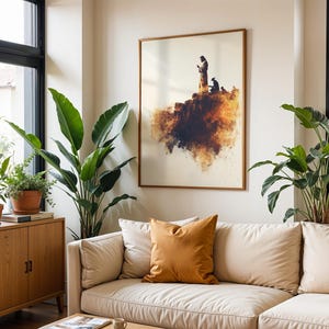 K&ouml;nnte beinhalten: Ein gerahmter Wandkunstdruck mit der Silhouette einer stehenden und einer knienden Figur auf einer felsigen Klippe, dargestellt in Braun-, Orange- und Cremet&ouml;nen mit Aquarell-Effekt, in einem d&uuml;nnen Holzrahmen pr&auml;sentiert.
