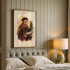 May include: A framed wall art print depicting a historical figure wearing a dark cap and a fur-trimmed robe, holding an open book and a green palm frond. The figure has a golden halo behind their head, rendered in a watercolor style with warm tones.