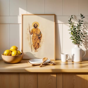 Op de afbeelding: Een ingelijste verticale kunstdruk met een bebaarde figuur in gouden gewaden die een staf vasthoudt met een aureool boven het hoofd. De print staat op een houten aanrecht naast een houten kom met gele citroenen, een wit bord, een houten lepel en een witte vaas.