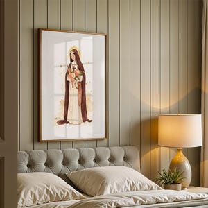 May include: A framed wall art print featuring a watercolor illustration of a figure in a long cream-colored habit and a dark brown cloak, holding a bouquet of pink and orange flowers with a small wooden cross, set against a white background.