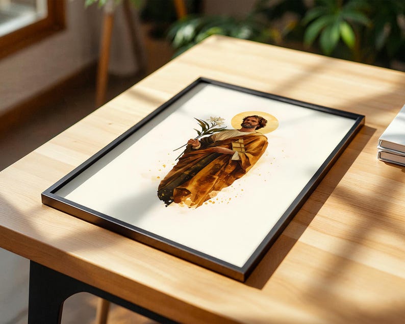 K&ouml;nnte beinhalten: Ein gerahmter Druck mit einer Aquarell-Illustration einer b&auml;rtigen Figur mit goldenem Heiligenschein, die ockerfarbene Gew&auml;nder tr&auml;gt und eine wei&szlig;e Lilie h&auml;lt. Das Kunstwerk ist auf cremefarbenem Grund mit Farbspritzern und dunklen R&auml;ndern.
