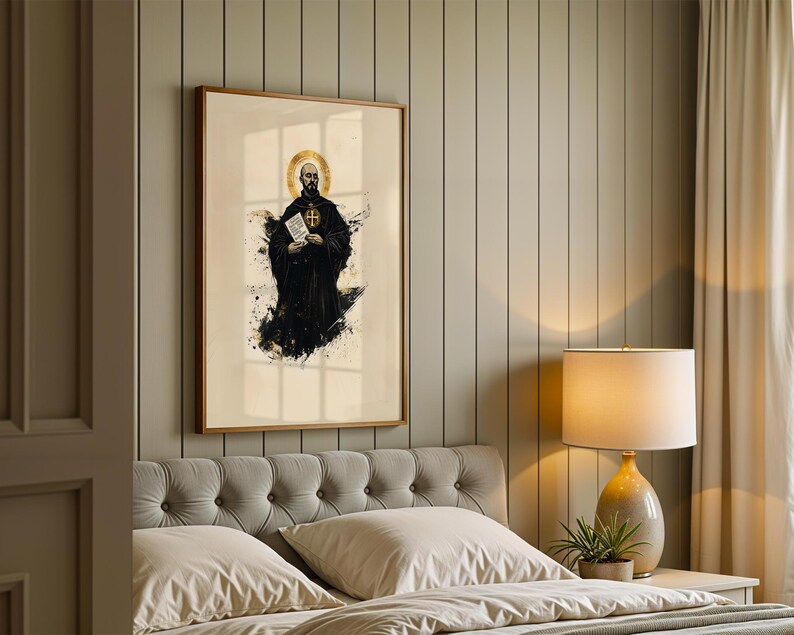 May include: A framed wall art print featuring a stylised illustration of a monk in a black habit with a gold halo, holding a white document. The artwork uses a cream background with black ink-like splatters and gold accents in a wooden frame.