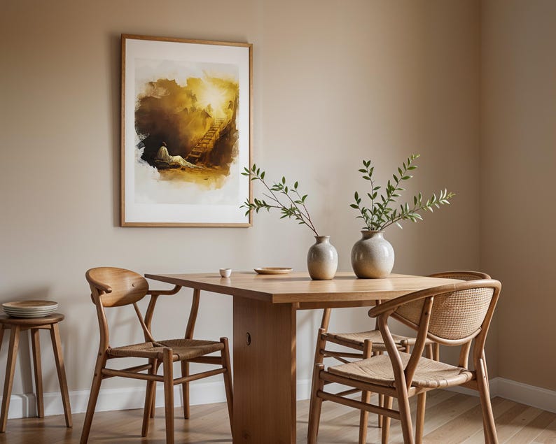 Op de afbeelding: Een rechthoekige ingelijste kunstdruk met een illustratie in aquarel-stijl van een figuur bij een ladder die naar een fel licht leidt. Het kunstwerk hangt boven een houten eettafel met twee keramische vazen en houten stoelen.