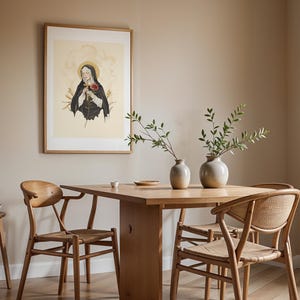 Op de afbeelding: Een ingelijste muurkunstprint met een figuur in een zwart habijt met een gouden aureool, die een houten kruis en een rode roos vasthoudt. De print hangt in een kamer met een houten eettafel en vier houten stoelen met gevlochten zittingen.