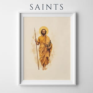 K&ouml;nnte beinhalten: Ein gerahmter Kunstdruck mit dem Text SAINTS am oberen Rand. Die Abbildung zeigt eine b&auml;rtige Figur in goldgelben Gew&auml;ndern, die einen langen Speer in der rechten Hand und eine Schriftrolle in der linken h&auml;lt, mit einem goldenen Heiligenschein.