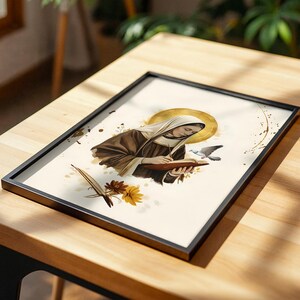 May include: A framed art print featuring a figure in a brown habit and white head covering writing in a book. A golden halo surrounds the head, with a small bird, a quill, and yellow and brown flowers depicted on a cream background.