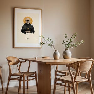 May include: A framed wall art print featuring a bald figure in a black hooded robe with a golden halo and a cross pendant, displayed above a wooden dining table with two light-colored ceramic vases containing green leafy branches and chairs.