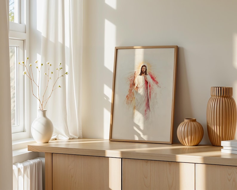 May include: A framed wall art print featuring a watercolor-style illustration of a figure with long hair and a beard, wearing white robes with red accents, surrounded by a golden halo, displayed in a light wood frame on a wooden surface.