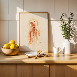 May include: A framed watercolor-style print depicting a figure with a crown of thorns holding a red rose, surrounded by a golden halo. The artwork is displayed on a counter next to a wooden bowl of yellow lemons, a white plate, a wooden spoon, and a vase.