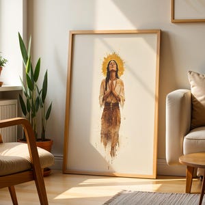 May include: A framed vertical wall art print featuring a watercolour-style illustration of a person with eyes closed and hands pressed together in prayer. The figure is centred with a golden halo behind the head, wearing earth-toned clothing.