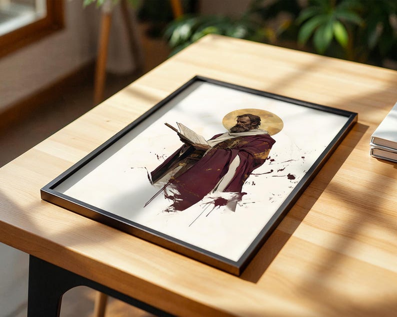 May include: A framed rectangular print featuring a bearded figure in a maroon robe holding an open book. The figure has a golden halo behind their head, set against a white background with dark red ink-like splatters and abstract brush strokes.
