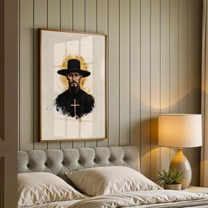 Puede incluir: Una impresi&oacute;n de arte mural enmarcada que presenta el retrato de una persona con barba, un sombrero negro de ala ancha y una prenda oscura con una cruz dorada, sobre un fondo circular de estilo acuarela en tonos dorados.