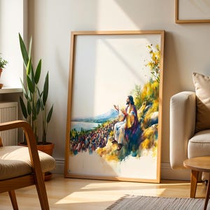 May include: A framed vertical wall art print featuring a watercolor-style illustration of a figure with long hair and a robe sitting on a hillside, gesturing toward a large crowd gathered below near a body of water, with yellow and blue tones.