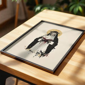 May include: A framed art print featuring a stylized illustration of a nun wearing a black habit and a crown of thorns. The figure holds a red book and a white lily against a cream background, accented by a gold halo and black ink splatters.