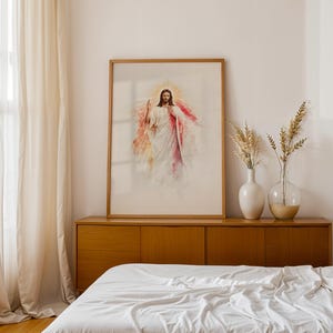 May include: A framed wall art print featuring a watercolor-style illustration of Jesus Christ with a glowing halo, wearing white and red robes. The artwork is displayed in a light wood frame, positioned on a wooden sideboard next to two glass vases.
