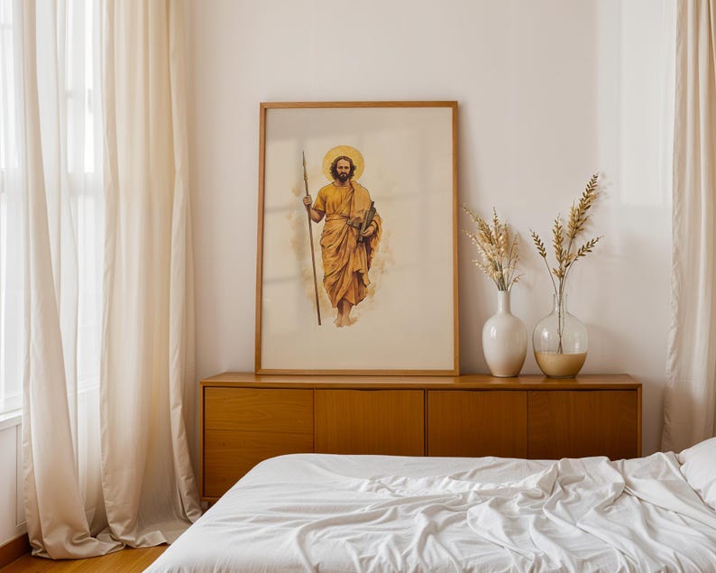 K&ouml;nnte beinhalten: Ein gerahmter vertikaler Wandkunstdruck mit einer Aquarellillustration einer b&auml;rtigen Figur in goldenen Gew&auml;ndern, die einen langen Speer und ein Buch h&auml;lt, mit einem kreisf&ouml;rmigen Heiligenschein hinter dem Kopf, in einem hellen Holzrahmen.