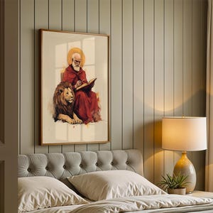 K&ouml;nnte beinhalten: Ein gerahmter Kunstdruck, der eine b&auml;rtige Figur in einem roten Gewand mit goldenem Heiligenschein zeigt, die in ein offenes Buch schreibt und neben einem L&ouml;wen sitzt. Die Illustration verwendet aquarellartige Pinselstriche und sanfte T&ouml;ne.