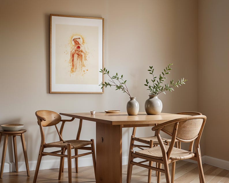 May include: A framed wall art print depicting a figure with a halo holding a red flower, displayed above a wooden dining table with two ceramic vases containing green leafy branches, accompanied by three wooden chairs with woven seats.