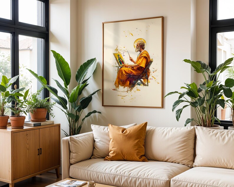 May include: A framed wall art print featuring a watercolour-style illustration of a bearded figure in orange robes sitting on a chair, holding a paintbrush and a small canvas depicting a portrait, set against a light cream background.