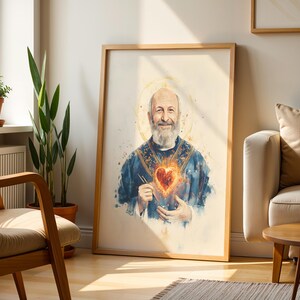 May include: A framed wall art print featuring a watercolor-style portrait of a bearded man with a golden halo, wearing a blue vestment and holding a glowing, fiery heart in his hands, set against a light, neutral-toned background.