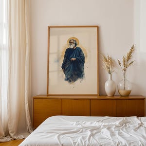 May include: A framed vertical wall art print featuring a watercolor-style illustration of a bearded figure with long hair wearing a dark blue robe, set against a soft beige background with a circular golden halo behind the figure's head.