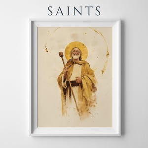 May include: A framed wall art print titled SAINTS featuring a watercolor-style illustration of a bearded figure in golden robes holding a wooden staff. The figure has a circular gold halo behind their head, set against a cream background.