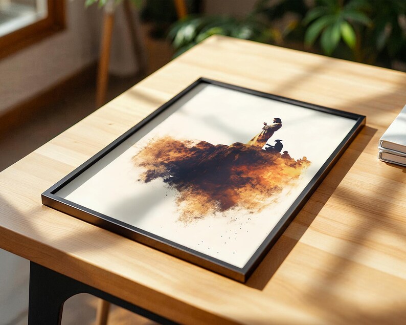 May include: A rectangular framed print featuring an artistic illustration of figures standing on a dark, textured, cloud-like formation. The artwork uses shades of brown, black, and cream, set within a thin black frame on a light wooden surface.