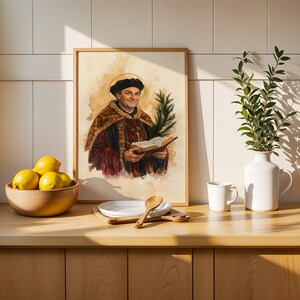May include: A framed watercolour-style print depicting a historical figure in a dark cap and fur-trimmed robe holding an open book and a palm frond. The artwork is displayed on a wooden counter alongside a bowl of yellow lemons and a white vase.