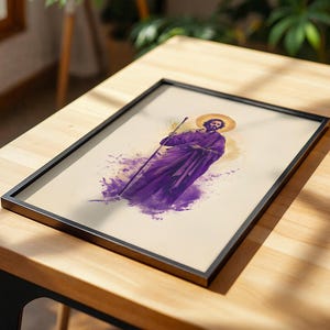 May include: A framed print featuring a stylized illustration of a bearded figure wearing a purple robe and holding a staff. The figure has a golden halo behind their head, set against a cream-colored background with purple watercolor-style accents.