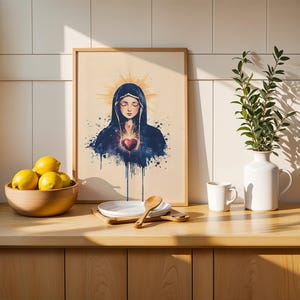K&ouml;nnte beinhalten: Ein gerahmter Kunstdruck mit einer Aquarell-Illustration einer Figur in einem dunkelblauen Kapuzenumhang mit einem leuchtend roten Herzen in der Mitte, umgeben von einem goldenen Heiligenschein auf hellbeigem Hintergrund.