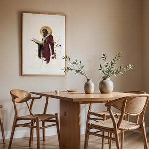 May include: A framed wall art print depicting a bearded figure in a deep red robe holding an open book with a gold halo, displayed above a light wood dining table with four chairs and two ceramic vases containing green leafy branches.