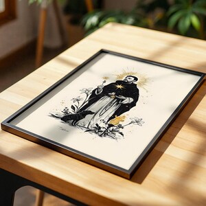 Op de afbeelding: Een ingelijste kunstdruk met een zwart-witillustratie van een figuur in een gewaad met een gouden aureool, die een klein voorwerp vasthoudt. Een hond staat bij de figuur, omringd door gestileerde lelies en een kleine vlam op een cr&egrave;mekleurige achtergrond.