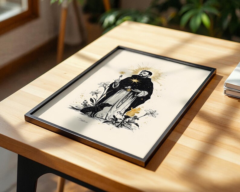 Op de afbeelding: Een ingelijste kunstdruk met een zwart-witillustratie van een figuur in een gewaad met een gouden aureool, die een klein voorwerp vasthoudt. Een hond staat bij de figuur, omringd door gestileerde lelies en een kleine vlam op een cr&egrave;mekleurige achtergrond.