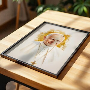 Pu&ograve; includere: Una stampa ritratto incorniciata raffigurante un'illustrazione in stile acquerello di Papa Giovanni Paolo II che indossa una veste bianca e una collana con crocifisso d'oro, su uno sfondo neutro con un morbido effetto alone circolare giallo oro.