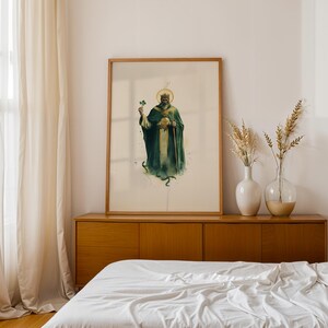 May include: A framed vertical art print featuring a watercolour illustration of a bearded figure wearing a crown and a dark green robe, holding a shamrock and a staff. The figure has a golden halo and stands above a small green snake.