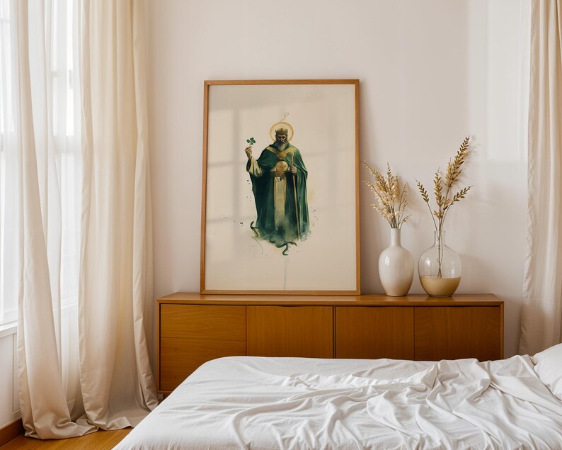 May include: A framed vertical art print featuring a watercolour illustration of a bearded figure wearing a crown and a dark green robe, holding a shamrock and a staff. The figure has a golden halo and stands above a small green snake.