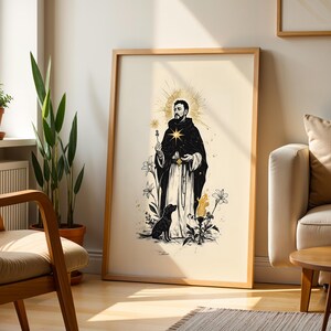 Op de afbeelding: Een ingelijste kunstdruk met een zwart-witillustratie van een bebaard figuur in een donkere kapmantel met een gouden ster op de borst, een aureool, een hond, lelies en een vlam, alles tegen een lichtcr&egrave;me achtergrond in een houten lijst.