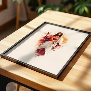 Puede incluir: Una l&aacute;mina de arte enmarcada que presenta una ilustraci&oacute;n estilo acuarela de Jesucristo con un Sagrado Coraz&oacute;n brillante. La figura viste t&uacute;nicas blancas y rojas sobre un fondo crema, dentro de un marco rectangular negro fino.