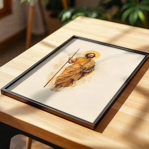 K&ouml;nnte beinhalten: Ein gerahmter Druck mit einer Illustration im Aquarellstil einer b&auml;rtigen Figur in goldenen Gew&auml;ndern, die einen langen Stab und ein Buch h&auml;lt. Die Figur hat einen kreisf&ouml;rmigen Heiligenschein hinter dem Kopf. Das Bild ist in einem d&uuml;nnen schwarzen Rahmen.