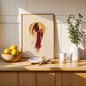 Puede incluir: Una l&aacute;mina de arte vertical enmarcada que muestra a una figura con una t&uacute;nica larga roja y blanca sosteniendo un frasco peque&ntilde;o frente a un gran fondo circular dorado. La l&aacute;mina est&aacute; sobre una encimera de madera junto a un bol de limones y un jarr&oacute;n.
