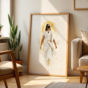May include: A framed vertical wall art print featuring a watercolor-style illustration of a figure with long hair and a beard, wearing white robes, looking upward with a golden halo effect behind the head, set against a light cream background.