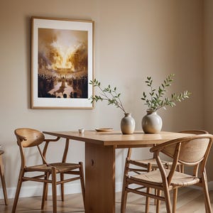 May include: A framed wall art print depicting a crowd gathered before a large structure engulfed in flames, displayed above a light wood dining table with four matching chairs featuring woven seats and two ceramic vases with green foliage.