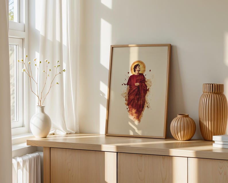 May include: A framed wall art print featuring a watercolour-style illustration of a figure in a deep red robe with a golden halo. The artwork is displayed in a light-toned wooden frame, showcasing a central portrait with abstract paint splatters.