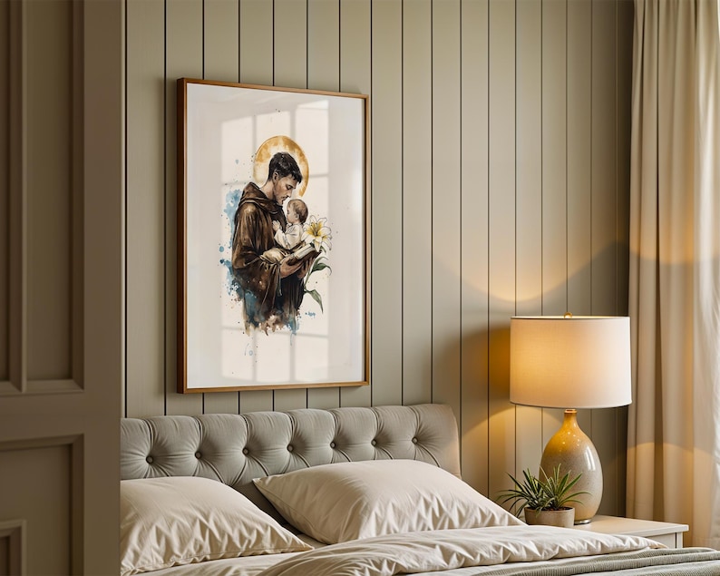 Puede incluir: Una impresi&oacute;n de arte mural vertical enmarcada que presenta una ilustraci&oacute;n en acuarela de una figura con t&uacute;nica marr&oacute;n que sostiene a un ni&ntilde;o peque&ntilde;o y un lirio blanco. Un halo circular dorado se coloca detr&aacute;s de la cabeza de la figura, con salpicaduras de pintura azul y marr&oacute;n.